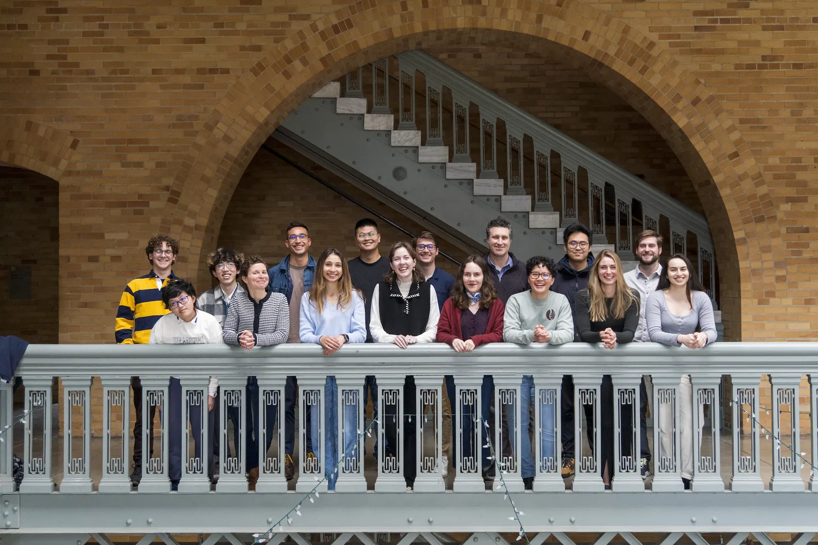 Members of the Minor Research Group standing along a balcony railing under a brick arch
